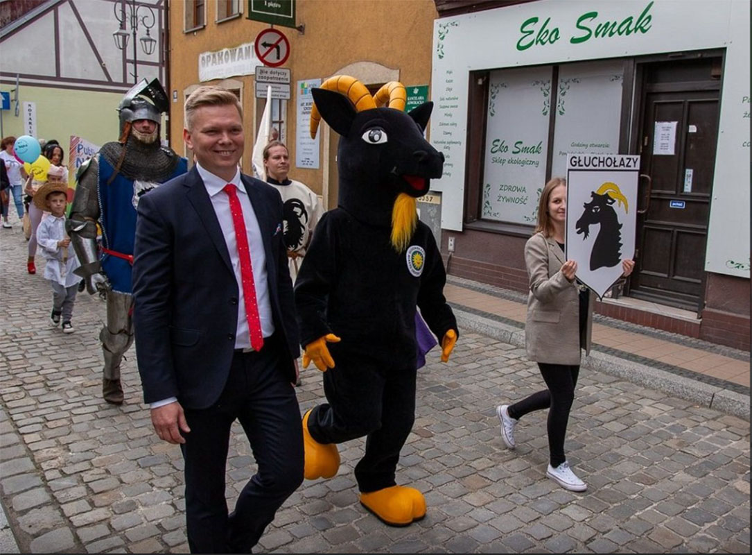 Na fotografii widnieje przebranie w postaci czarnej kozy pozujący do fotografii w trakcie przechadzki ulicami Głuchołaz